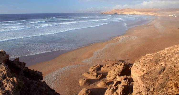 Weitläufiger Strand mit sanften Wellen unter klarem Himmel.