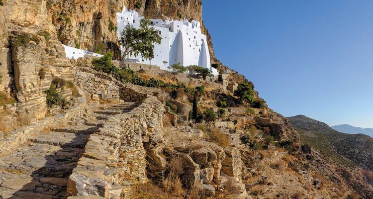 Monastère blanc construit dans une falaise avec un ciel bleu clair.