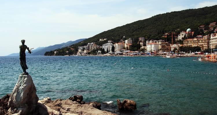 Vue côtière pittoresque avec une statue et la ville d'Opatija en arrière-plan.