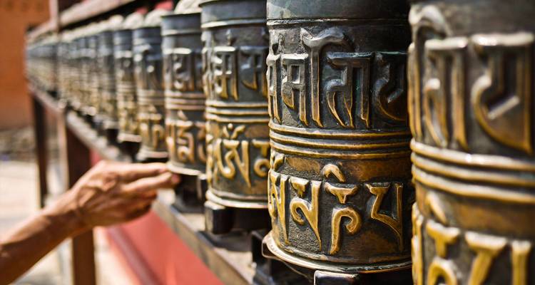 Hand, die eine Reihe von verzierten Gebetsmühlen mit Text in einem Tempel dreht.