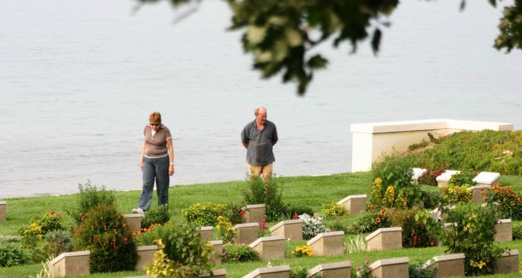 Menschen, die durch einen gepflegten Parkfriedhof am Meer spazieren.