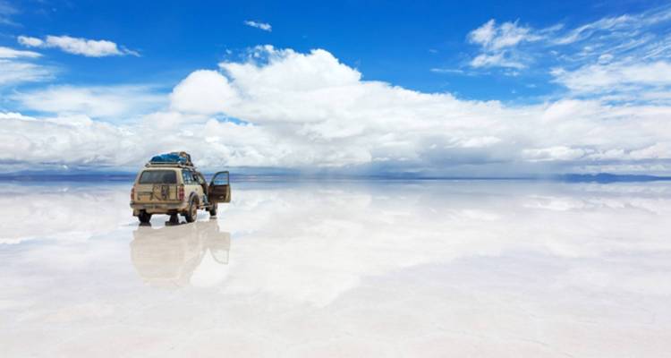Een 4x4 voertuig op het reflecterende oppervlak van de Uyuni Zoutvlakte onder een heldere hemel.