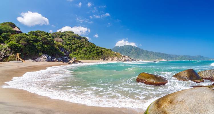 Una playa pintoresca con aguas turquesas y exuberantes colinas verdes al fondo.