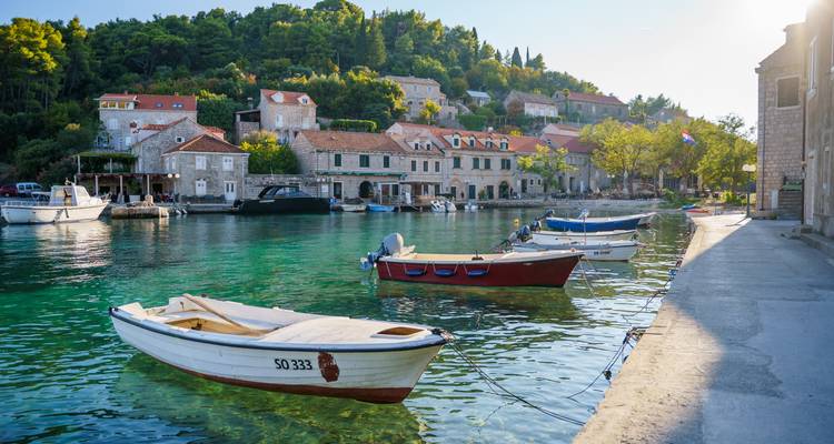 Village adriatique pittoresque avec des maisons en pierre et de petits bateaux flottant sur une eau bleu-vert cristalline sous le soleil de fin d'après-midi.
