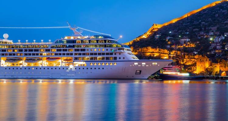 Navire de croisière amarré dans un port au crépuscule avec des structures illuminées.