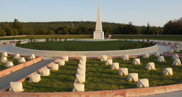 Circular memorial with a pointed obelisk surrounded by trees.