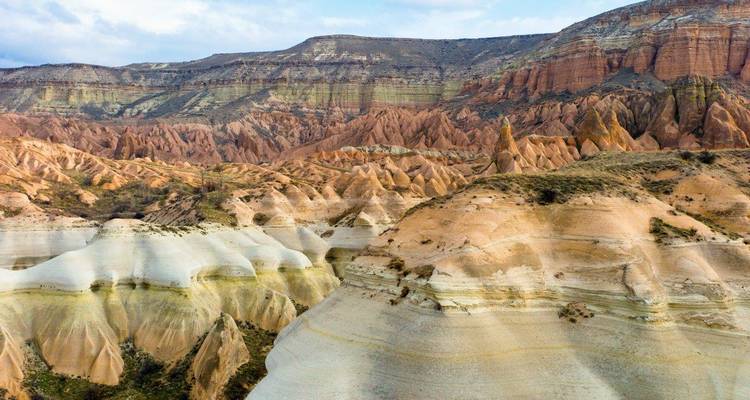 Multicolored banded rock ridges and spires stretching across a vast Cappadocian valley under patchy clouds.