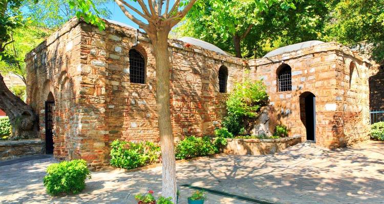 Stone chapel set among shady trees with bright flowers and dappled sunlight in a peaceful courtyard.