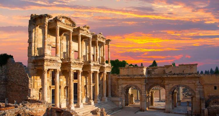 Ancient Library of Celsus ruins glowing under a vivid orange-pink sunset sky, revealing intricate Roman architecture.