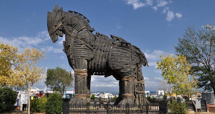 Large wooden replica of the Trojan Horse displayed outdoors in a park setting with blue skies above.