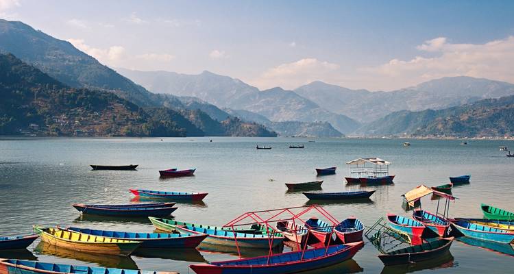 Bunte Boote auf einem See mit Bergen im Hintergrund.