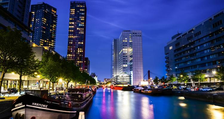 Rotterdam skyline tijdens de nacht met verlichte gebouwen en boten.
