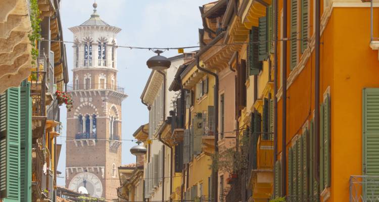 Smalle Italiaanse straat met kleurrijke gebouwen met luiken, met een hoge bakstenen klokkentoren die in de achtergrond uittorent.