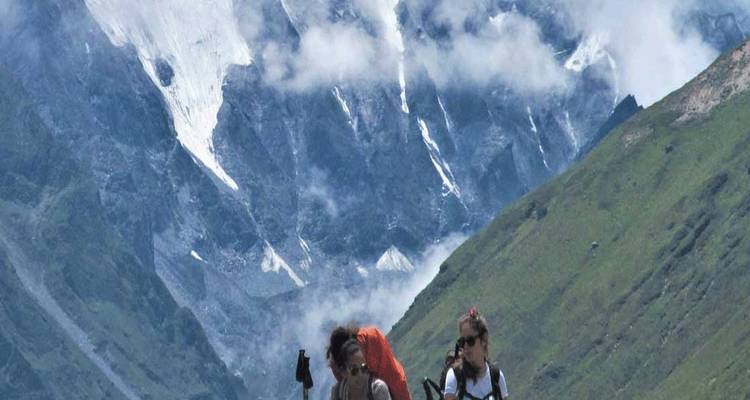 Dos mochileros caminan por un sendero alpino con montañas cubiertas de glaciares elevándose detrás de ellos.