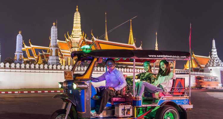 Ein Tuk-Tuk mit Menschen vor einem beleuchteten Tempel.