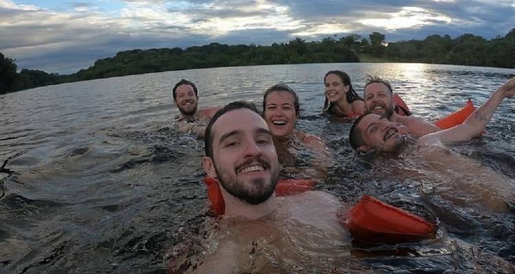 Groupe d'amis souriant et flottant dans une rivière au coucher du soleil avec des gilets de sauvetage.