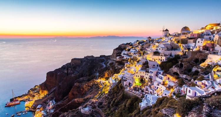 Atardecer mágico sobre el pueblo de Oia en acantilados iluminados con el tranquilo mar Egeo extendiéndose hasta el horizonte