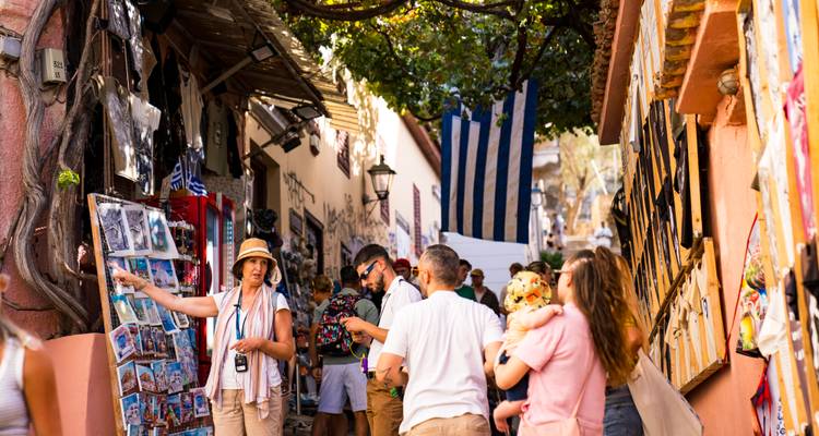 Callejón peatonal animado lleno de souvenirs y con sombra de árboles, turistas mirando y charlando