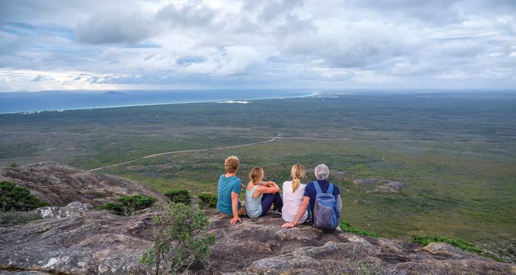 Grupo de personas sentadas en un mirador con vista a un vasto paisaje y océano.