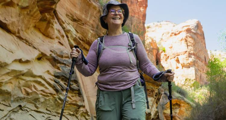 Excursionista sonriente con bastones de trekking caminando por un cañón de arenisca colorido.