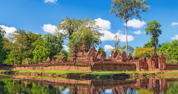 Oude tempel omringd door bomen en een reflecterende vijver.