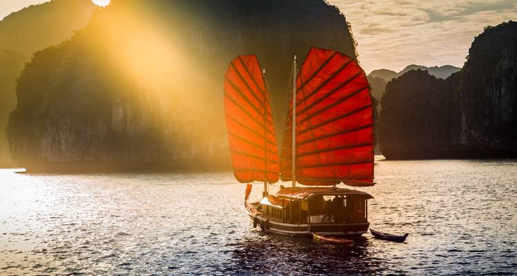 Traditionele Aziatische boot met rode zeilen op het water tijdens zonsondergang.