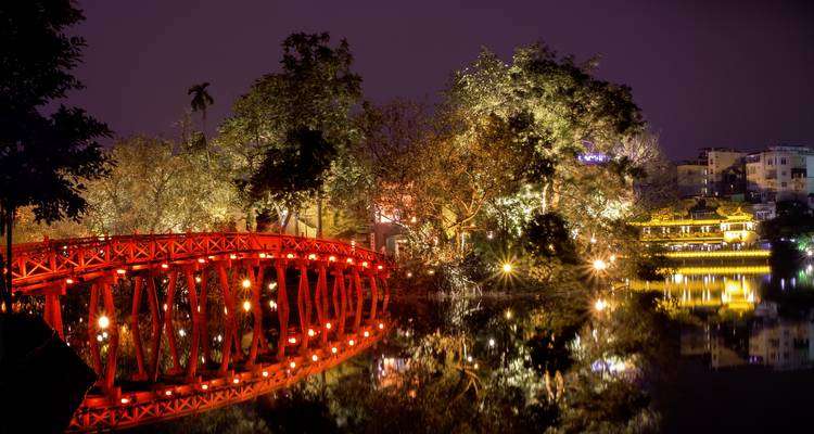 Verlichte brug en park met reflecties in het water 's nachts.
