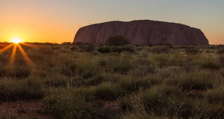 La formation rocheuse emblématique d'Uluru se détachant en silhouette contre un coucher de soleil lumineux avec des rayons de soleil.