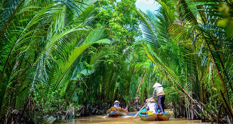 Small boats navigating through a lush river canal surrounded by palms.
