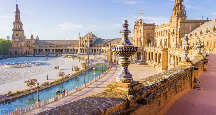 Grand semicircular plaza with ornate ceramic balustrades, canal, and historic Spanish buildings under warm sunlight
