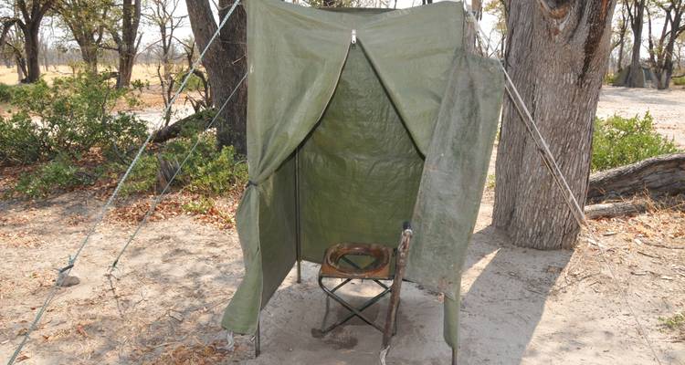 Tienda de campaña improvisada de lona en un área de acampada con árboles alrededor.