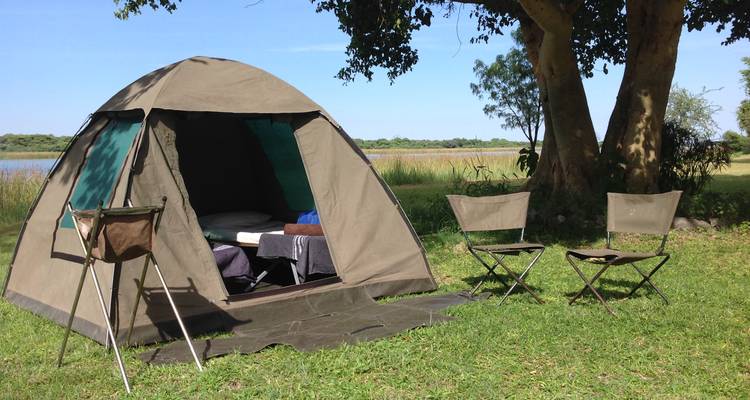 Tente et chaises de camping sur l'herbe avec vue sur un lac.