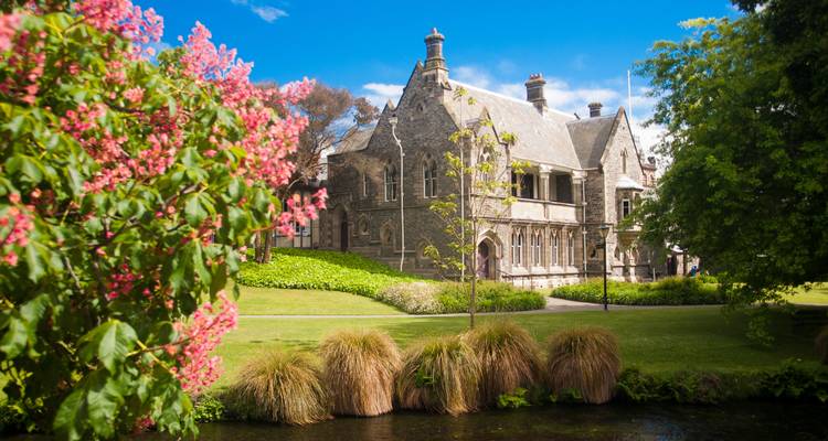 Historic stone building framed by blooming pink trees and lush gardens in Christchurch.