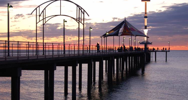 Un muelle recortado contra un cielo de atardecer vivido con el mar tranquilo reflejando colores suaves.