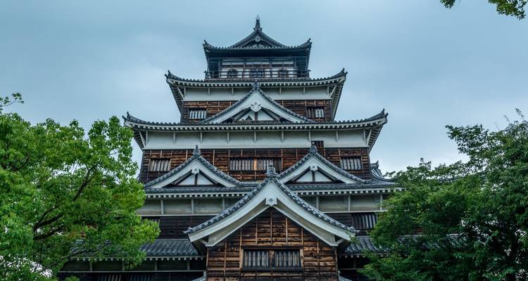 Un château japonais historique entouré de verdure sous un ciel nuageux.