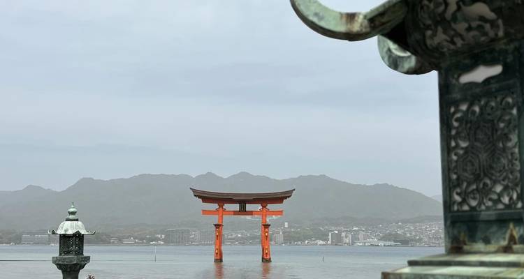The iconic vermilion torii of Itsukushima Shrine rises from calm sea with mountains behind.