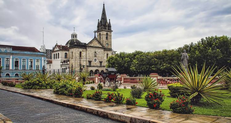 Iglesia histórica y carruaje enmarcados por jardines paisajísticos en un pueblo brasileño colonial.