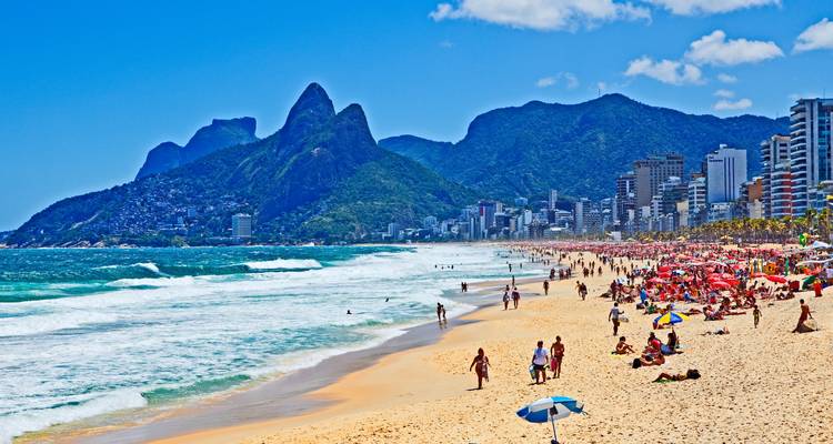 Playa de Ipanema llena de vida con el horizonte de la ciudad y los icónicos picos de los Dos Hermanos en Río de Janeiro.