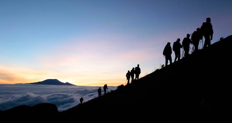 Excursionistas silueteados contra un horizonte crepuscular en una montaña.