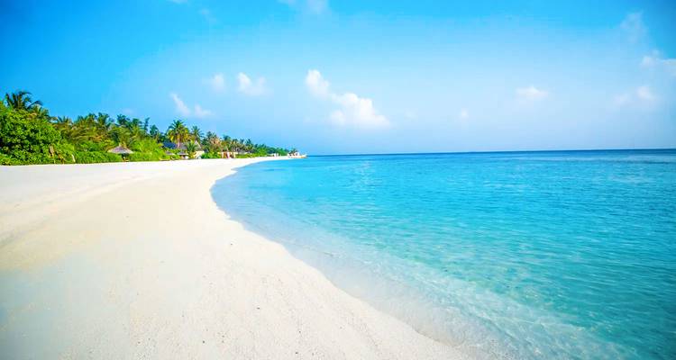 Weißer Sandstrand mit türkisfarbenem Wasser und klarem blauem Himmel.