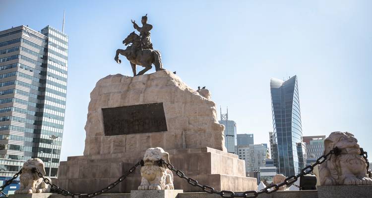 Estatua ecuestre sobre pedestal de piedra rodeada de modernos edificios de gran altura en una plaza de la ciudad
