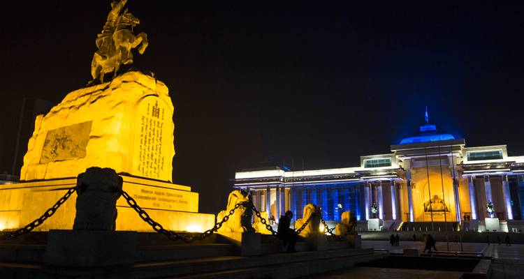 Plaza de la ciudad iluminada por la noche con monumento resplandeciente y edificio gubernamental