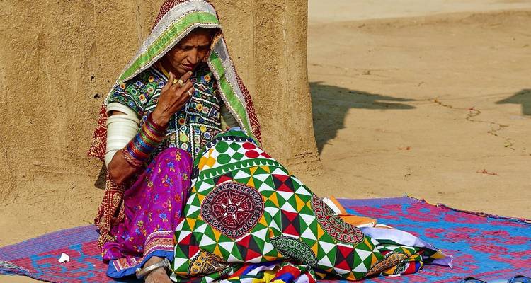 Frau in traditioneller bunter Kleidung beim Sticken.