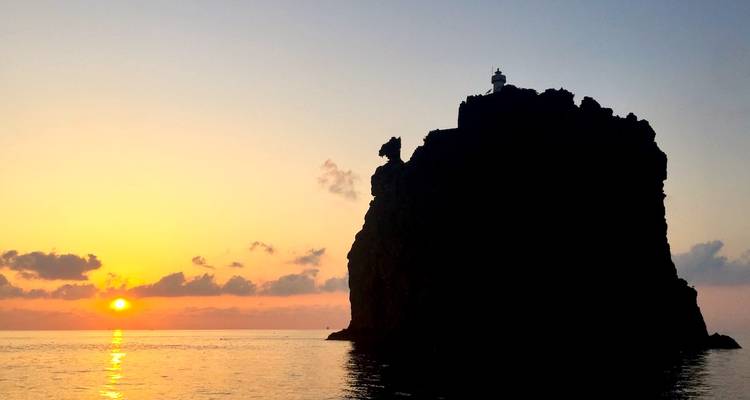 Silhouette d'une île rocheuse avec un phare au coucher du soleil.