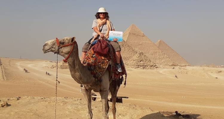 Person, die auf einem Kamel reitet und ein Schild hält, mit Pyramiden im Hintergrund