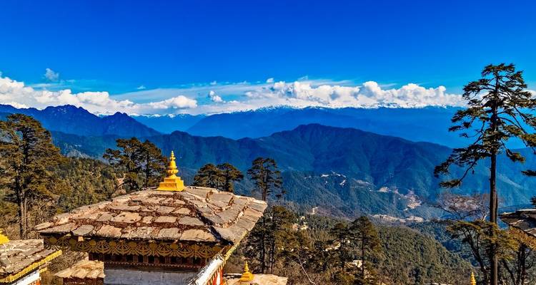 Verre zicht op een bergketen met traditionele Bhutaanse architectuur op de voorgrond.