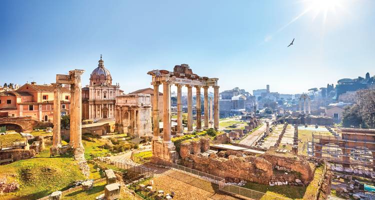 Les ruines ensoleillées du Forum romain avec des colonnes imposantes et des arcs anciens sur un ciel bleu éclatant.