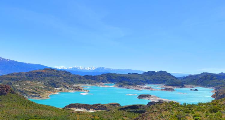 Weitläufige Aussicht auf einen türkisfarbenen See, umgeben von bergigem Gelände.