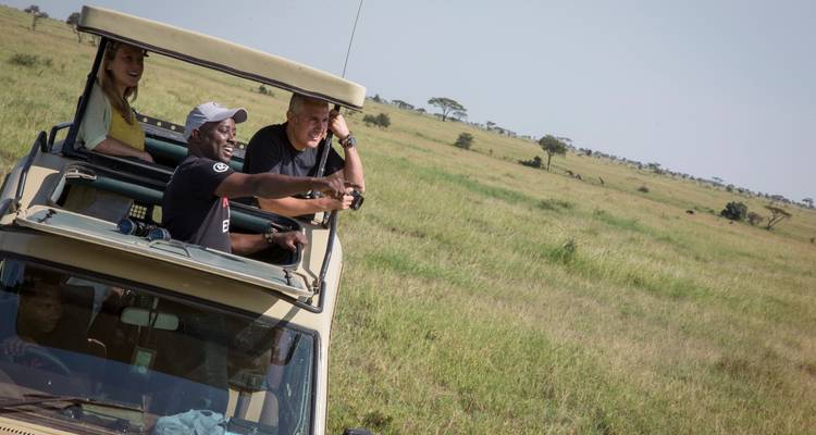 Un guía de safari señalando la vida silvestre desde la escotilla del techo de un vehículo 4x4 en la sabana abierta.