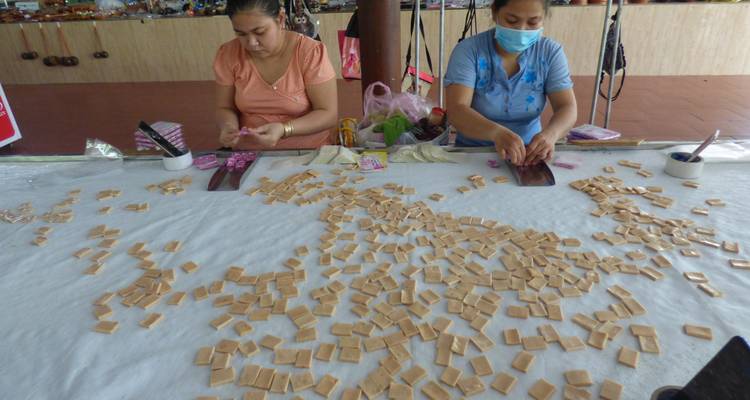 Dos mujeres haciendo artículos tradicionales en una mesa llena de artesanías.